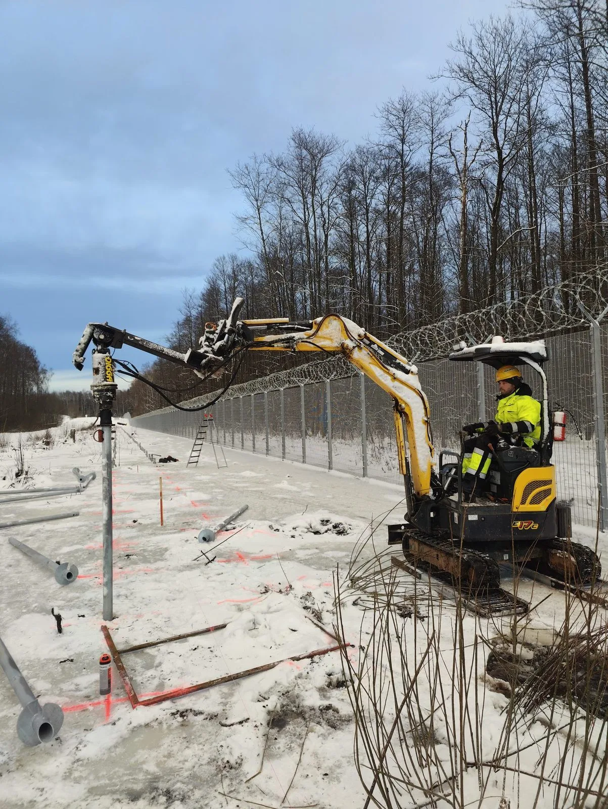 Minigrävmaskin installerar en skruvpåle i frusen mark